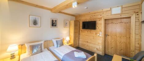 A hotel room with two beds, wooden walls, a TV, and a small table with a chair.