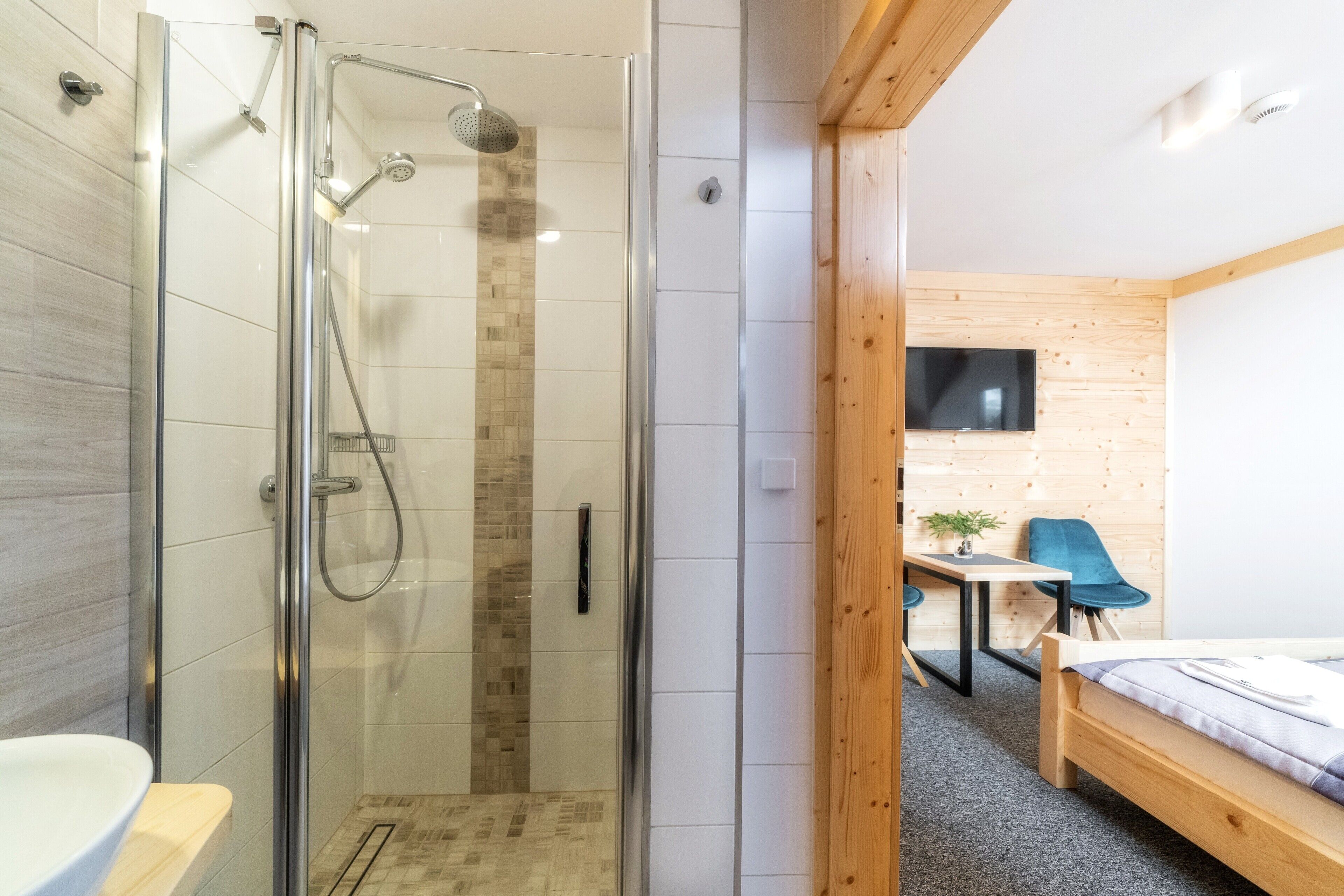 Un baño moderno con cabina de ducha de vidrio, un escritorio de madera, una silla y una cama con estructura de madera.