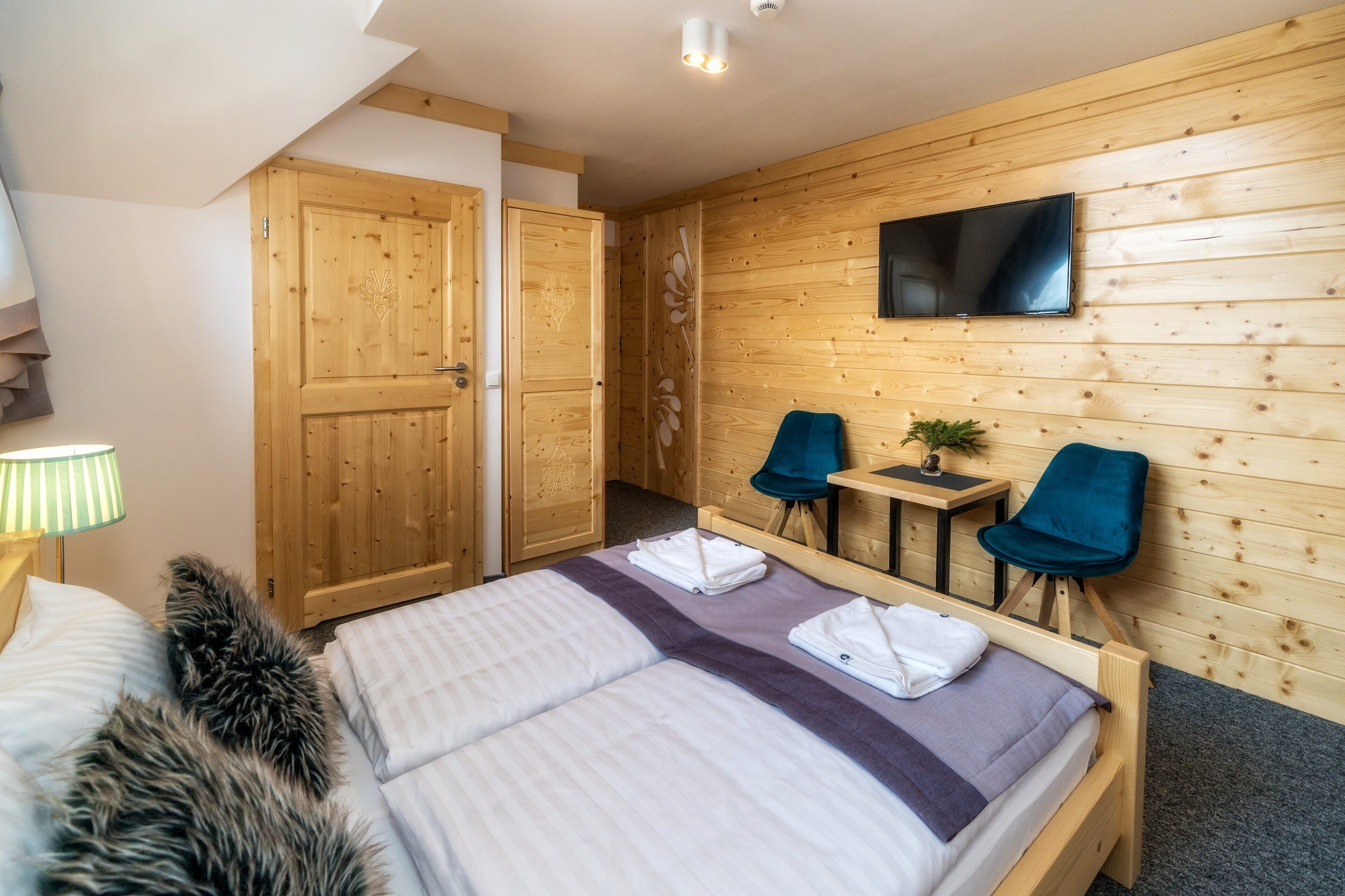 Una habitación con paneles de madera, una cama, un televisor y dos sillas.