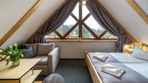 A cozy attic bedroom with a bed, a sofa, a small table, and a window with curtains. - Kaplowa Chata (Zakopane)