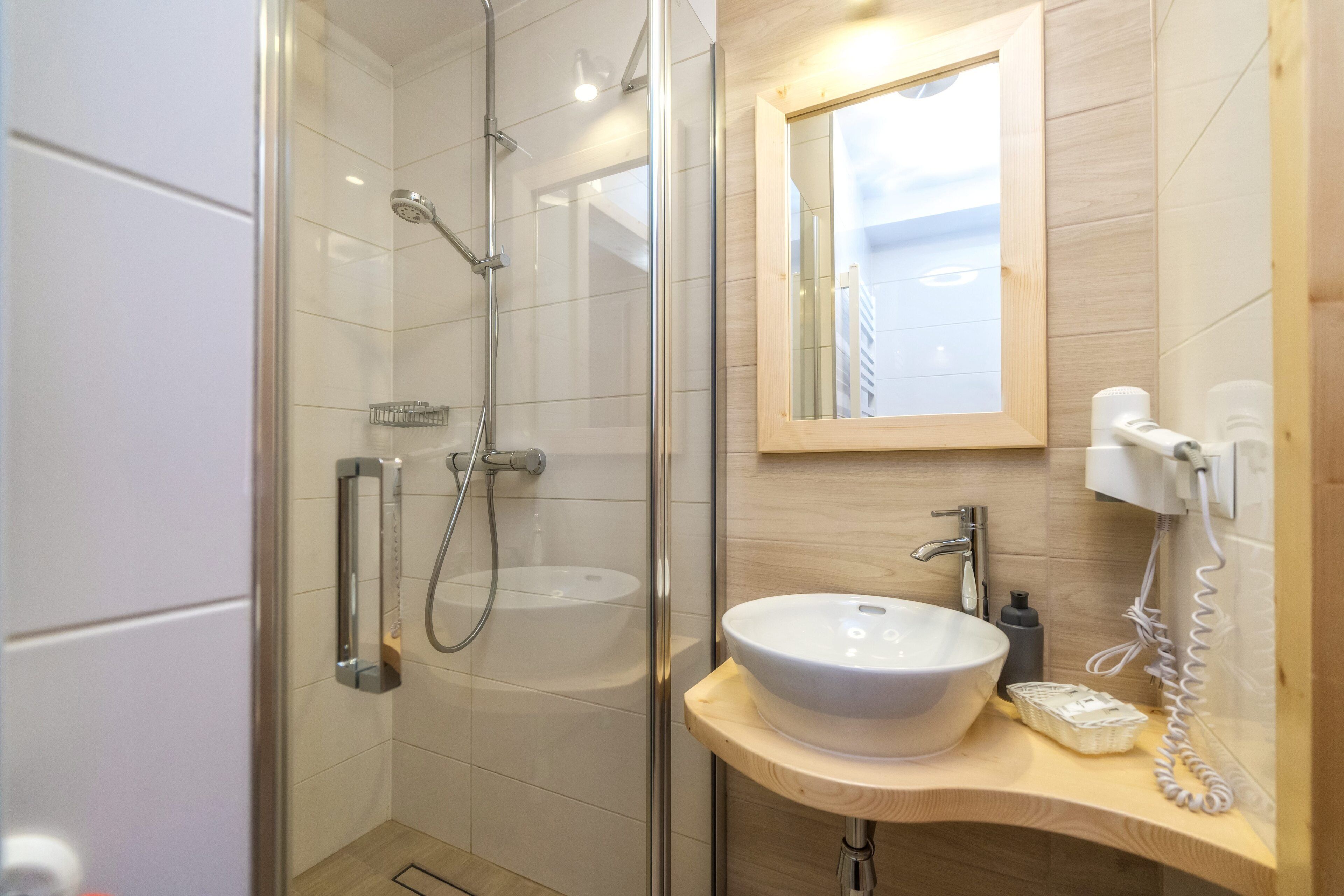 Ein modernes Badezimmer mit einer gläsernen Duschkabine, einem weißen Waschbecken und einem Holzlagerflächen.