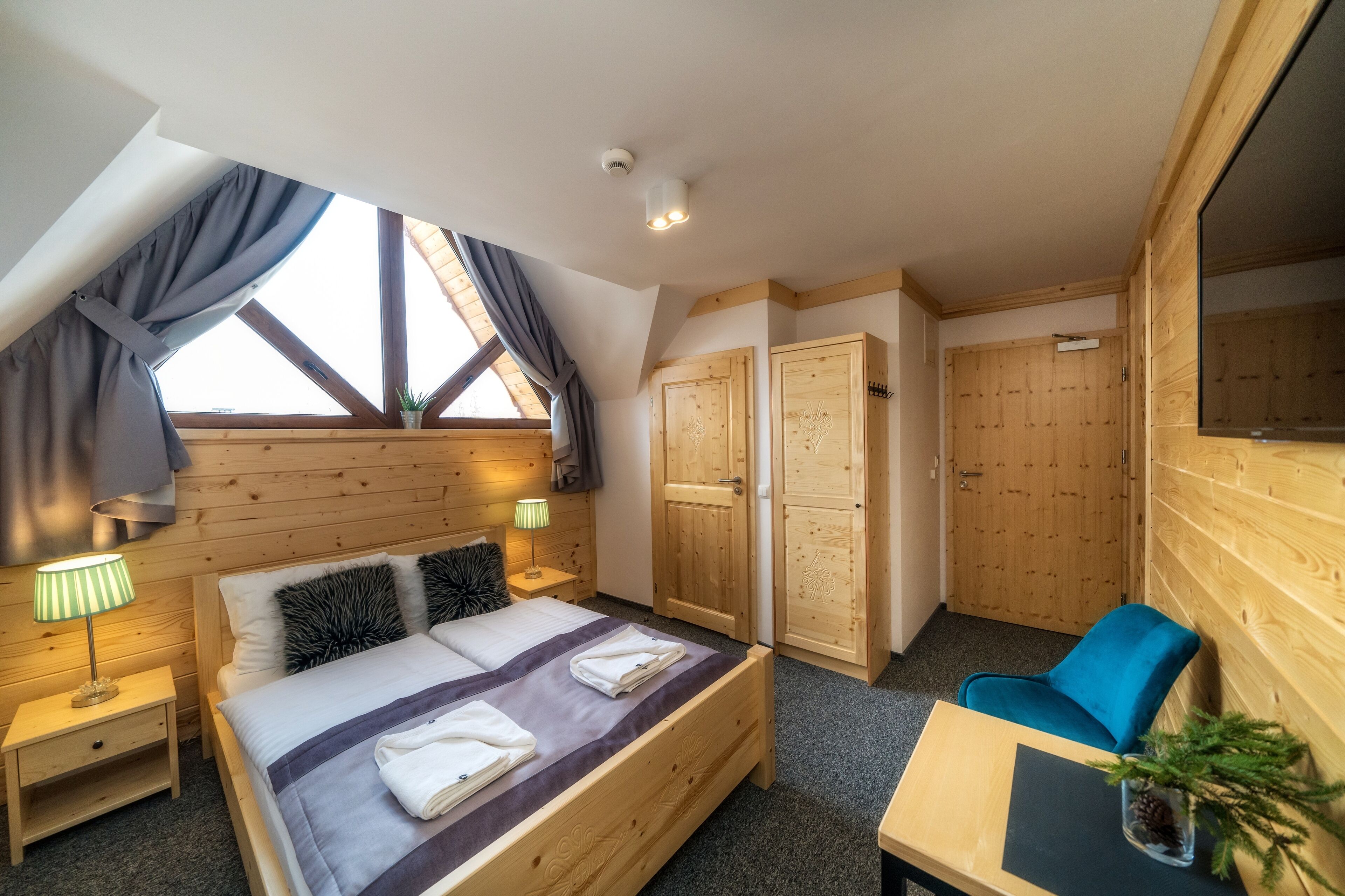 A bedroom with a wooden bed, a desk, a chair, and a window with curtains.