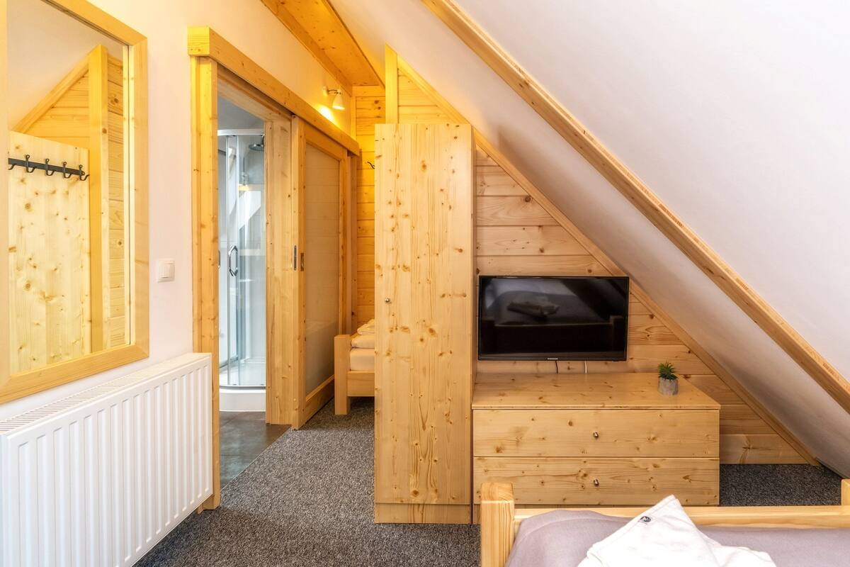 A wooden room with a TV mounted on a wall, a bed, a small dresser, and a mirror.