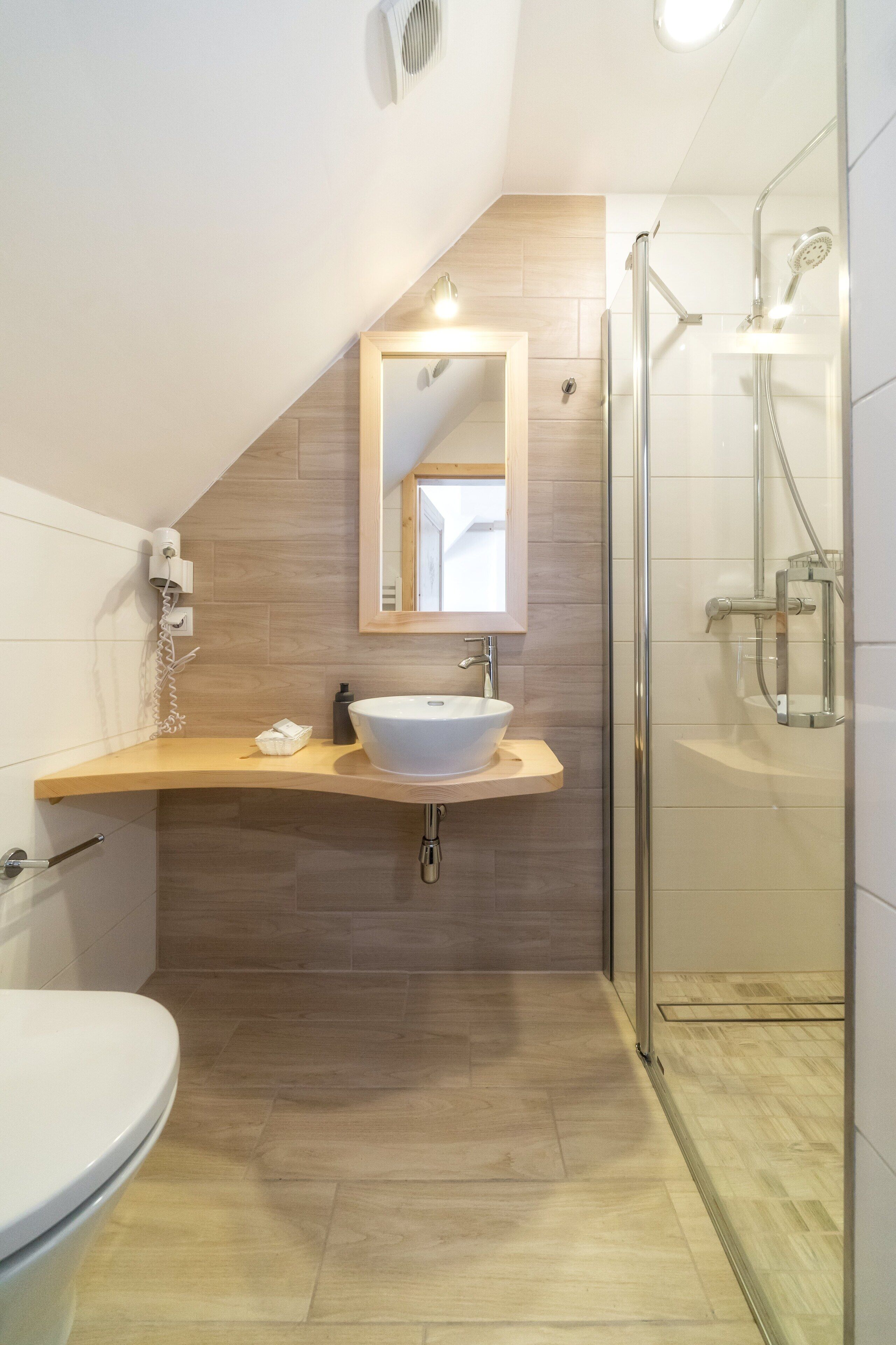 Une salle de bain moderne avec un meuble-lavabo en bois, un lavabo blanc, une cabine de douche en verre et des toilettes.