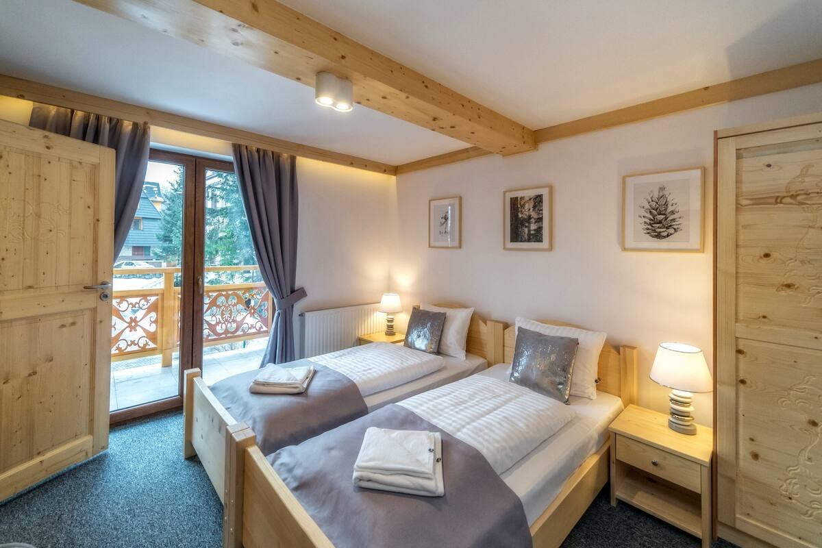 A double room with two beds, a wooden ceiling, a balcony with a railing, and a door.