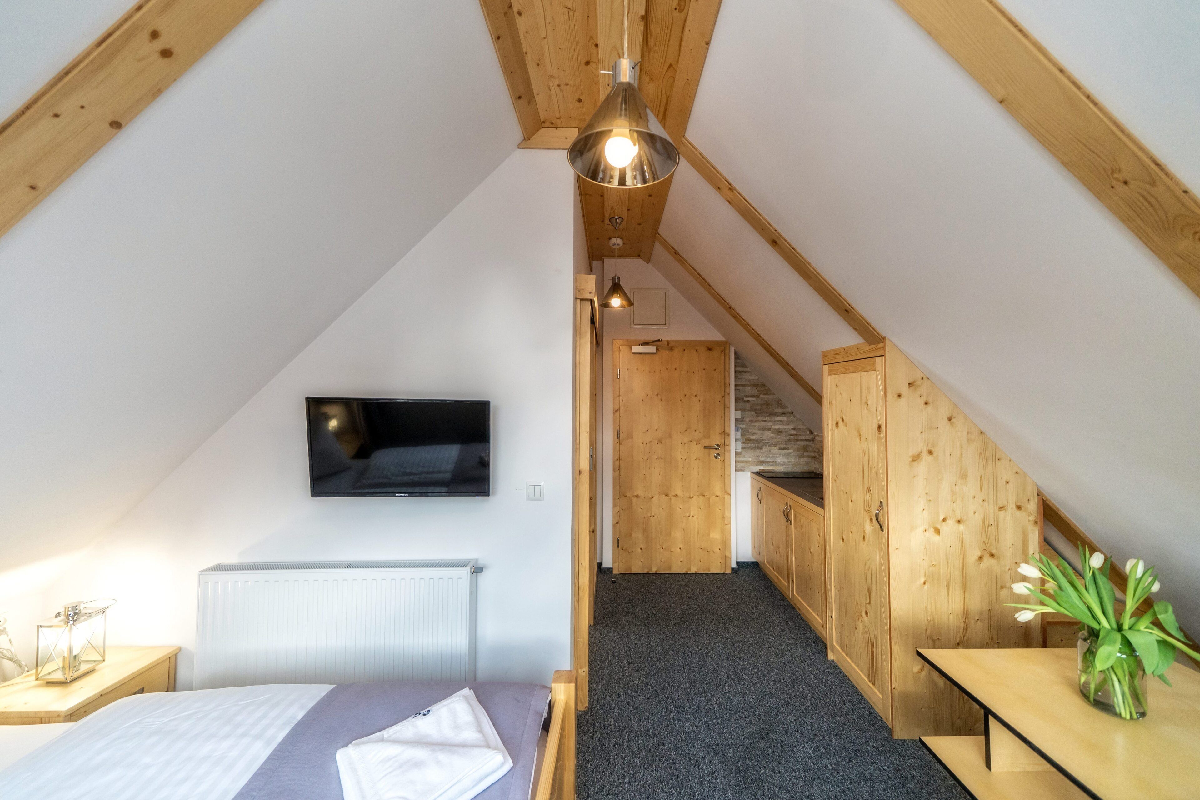Une chambre à coucher comprenant un lit, une table de chevet, un téléviseur fixé au mur et un escalier en bois menant à une autre pièce.