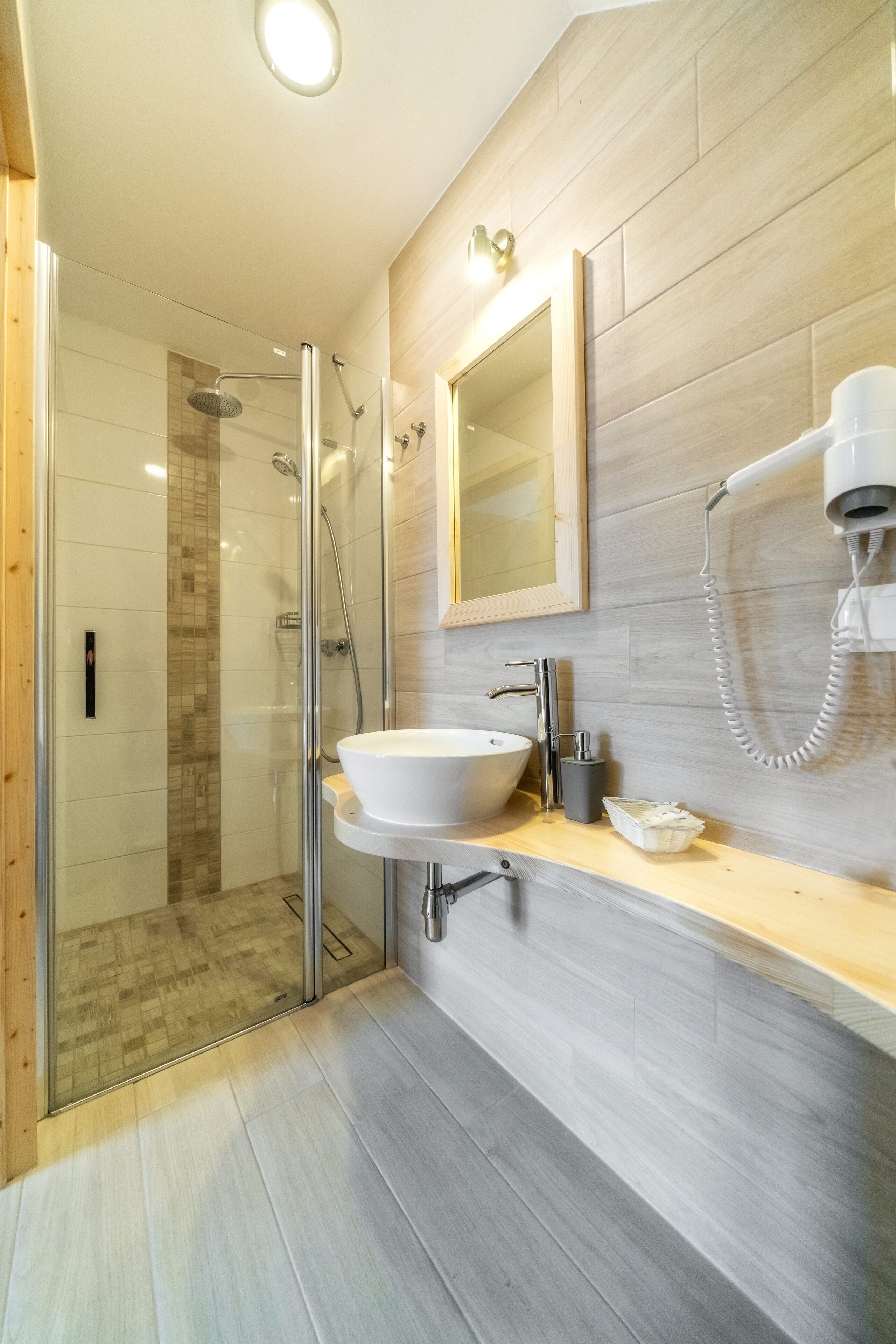 Un baño moderno con ducha envuelta en vidrio, un lavamanos blanco y un secador de pelo montado en la pared.