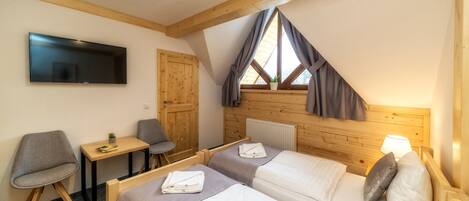 A bedroom with two beds, a TV, a desk, and a window with curtains.