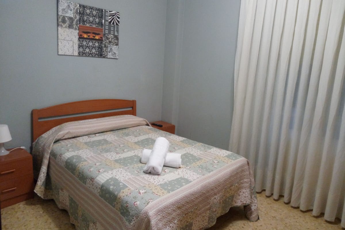 A bedroom with a wooden bed, a nightstand, a lamp, a quilt, and a window with curtains.