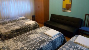 A room with two beds, a sofa, a television, and a wardrobe. - Pensión Cinco Villas (Logroño)