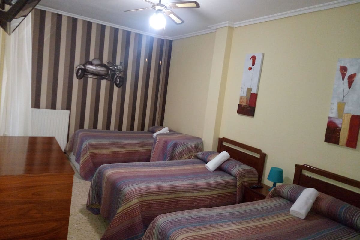 A hotel room with two beds, a wooden table, a ceiling fan, striped wallpaper, and abstract wall art.
