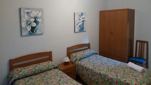 A bedroom with two beds, a wardrobe, and two wall-mounted paintings. - Pensión Cinco Villas (Logroño)