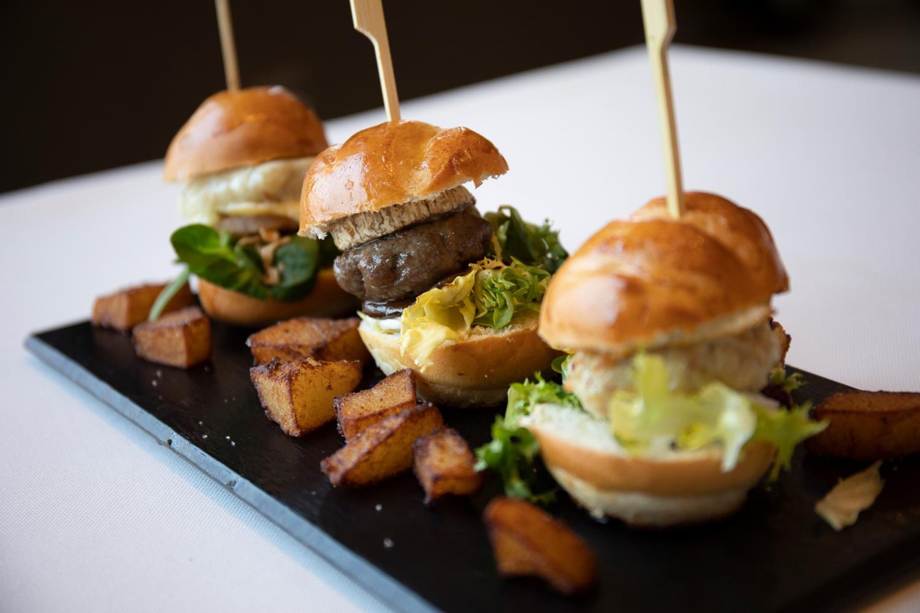 Tres hamburguesas con palillos, acompañadas de papas fritas en un plato negro.