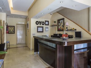 A reception area with a reception desk, a framed artwork, a fire extinguisher, and a door in the background. - Hotel El Mesón (Torrijos)