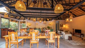 A dining area with wooden tables and chairs, a thatched ceiling, and hanging wicker lamps. - Hornbill Lodge (Kariba)