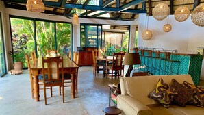 A spacious living area with a sofa, dining table, and chairs. There are large windows providing a view of greenery outside. - Hornbill Lodge (Kariba)