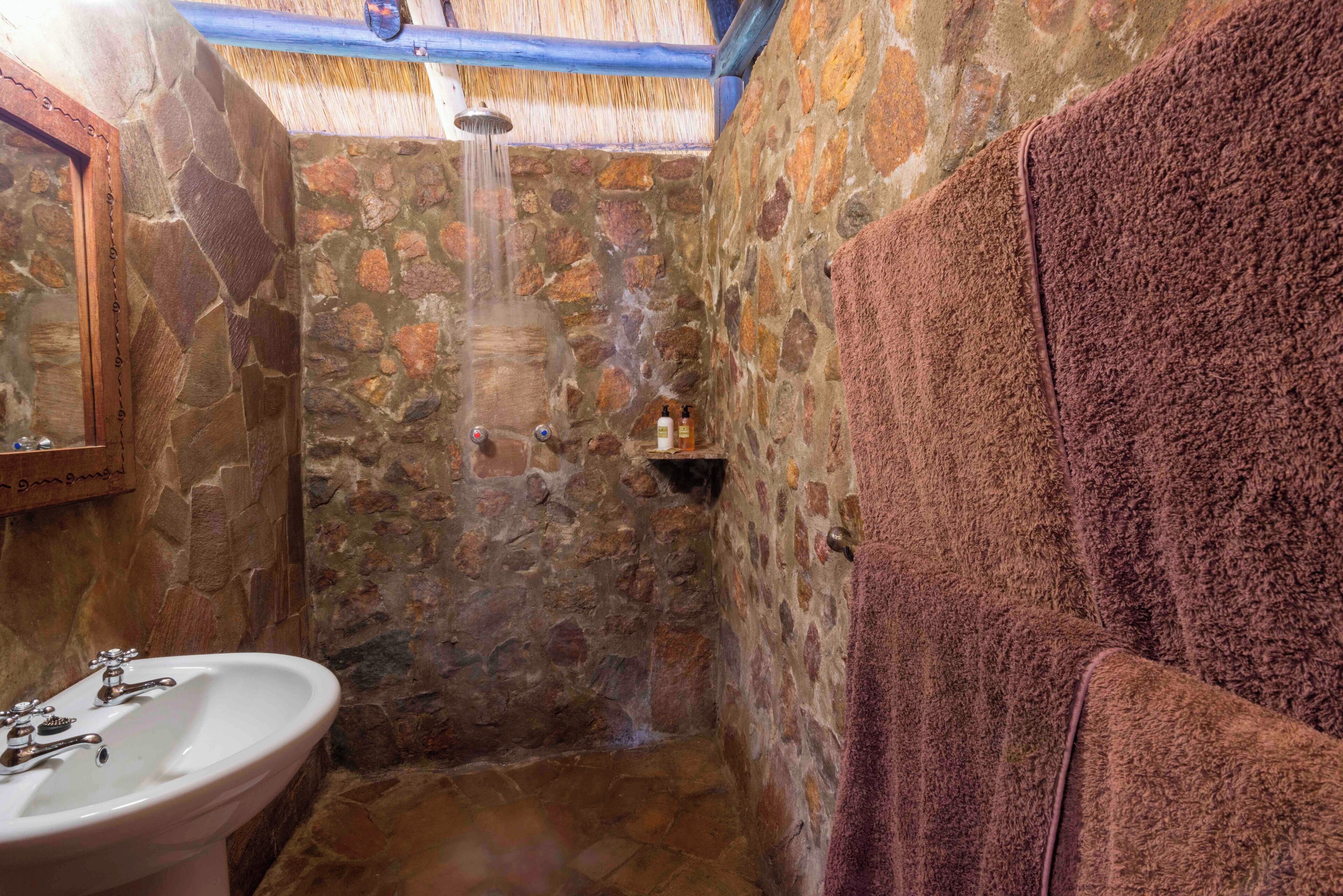 A stone-walled bathroom with a shower, a sink, and a towel rack.