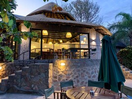 Un edificio rústico con techo de paja, paredes de piedra y un comedor con mesas al aire libre.