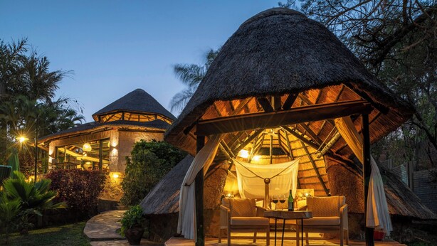 A thatched-roof structure with a seating area and a stone pathway leading to it. - Hornbill Lodge (Kariba)