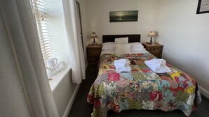 A neatly arranged bedroom with a bed, two bedside tables, a window with curtains, and a wall-mounted lamp. - The Anchor Hotel (Montrose)