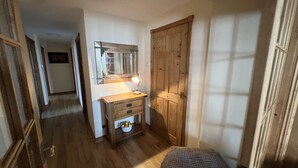 A narrow hallway with wooden flooring, a wooden desk with a mirror and a lamp, and a door on the right. - The Anchor Hotel (Montrose)
