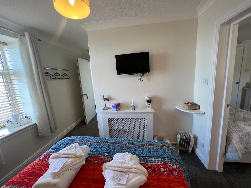 Habitación de hotel con cama, televisor montado en la pared, mesita de noche y ventana con cortinas.