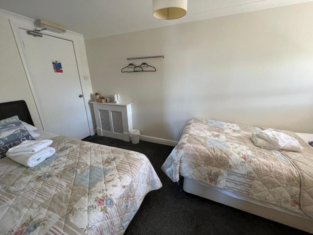 Et hotelværelse med to senge, en dør, et lille bord med et håndklæde og en knagerække.