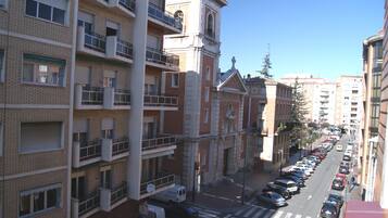 Un edifici de diverses plantes amb balcons, una construcció semblant a una església i un carrer amb cotxes aparcats.