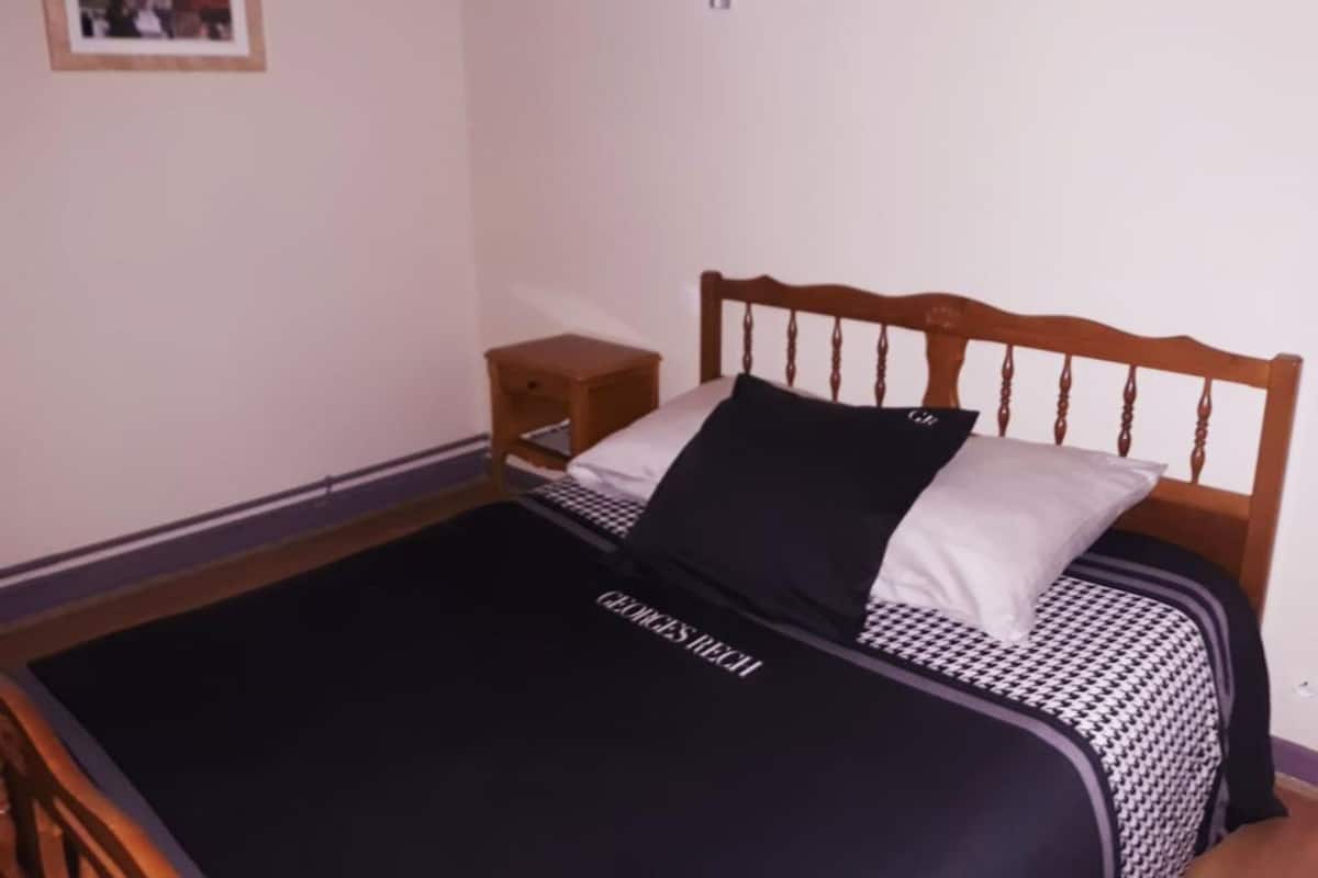 Una cama bien hecha con una colcha a cuadros blancos y negros, un cabecero de madera y una mesita de noche con una lámpara.