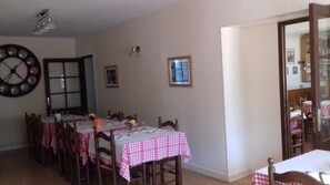 Un comedor con una mesa redonda preparada para cuatro personas, un reloj en la pared y una puerta que da a otra habitación.