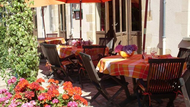Eine Terrasse im Freien mit Tischen, Stühlen, einem großen Sonnenschirm und verschiedenen Blumen.