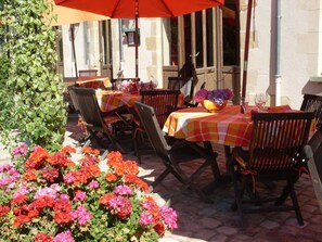An outdoor patio with tables and chairs, a large umbrella, and a variety of flowers. - Auberge Saint Aubin (Saint-Aubin-le-Monial)