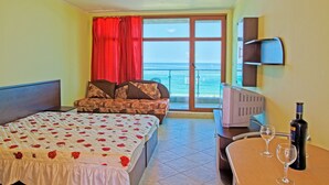 A hotel room with a bed, a sofa, a TV, a table with glasses, and a bottle. - Black Sea Paradise (Sozopol)