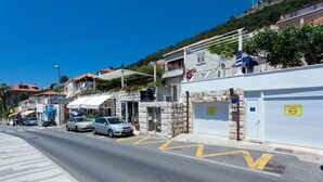 A street view with parked cars, a building with a stone facade, and a clear blue sky. - Apartments Cable car (Dubrovnik)