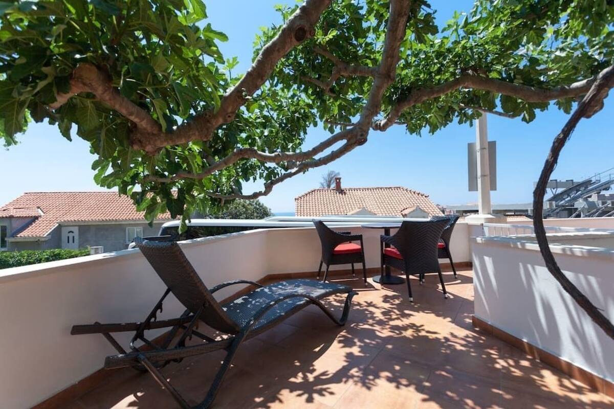 Une terrasse sur le toit, avec deux chaises et une table, d’où l’on peut admirer un quartier résidentiel aux toits recouverts de tuiles rouges.