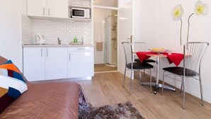 A compact room with a kitchenette, a dining area with two chairs, a bed, and a shower. - Apartments Cable car (Dubrovnik)