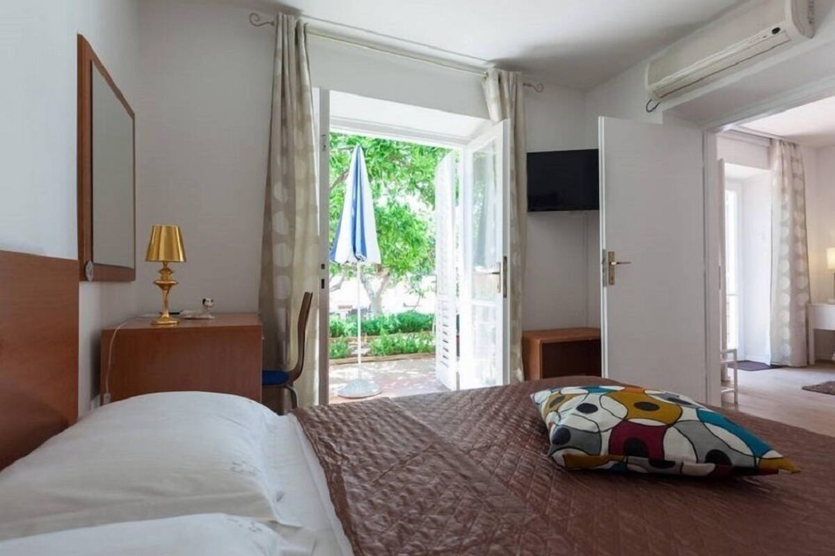 Une chambre d’hôtel avec un lit, un bureau doté d’une lampe, une télévision et une porte ouverte donnant sur un balcon.