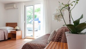 A hotel room with a bed, a nightstand, a lamp, a potted orchid, and a sliding glass door leading to an outdoor area. - Apartments Cable car (Dubrovnik)