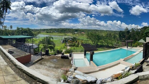 A swimming pool with a view of a lush landscape, a covered seating area, and a small waterfall feature. - Vinewoods Resorts by Cocotel (Taal)