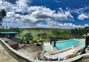 Una piscina con vistas a un paisaje exuberante, un área de descanso techada y una pequeña cascada.