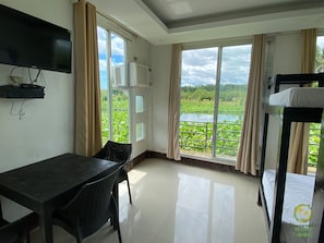 A room with a table, chairs, a bunk bed, a TV, and large windows with curtains. - Vinewoods Resorts by Cocotel (Taal)
