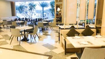 A spacious restaurant with multiple dining areas, including booths and tables, and a view of trees and buildings outside.