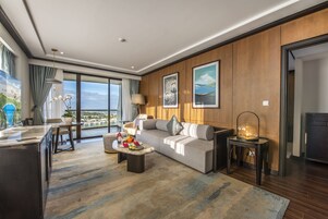 A modern hotel room with a large sofa, a dining area, and a view of the city.