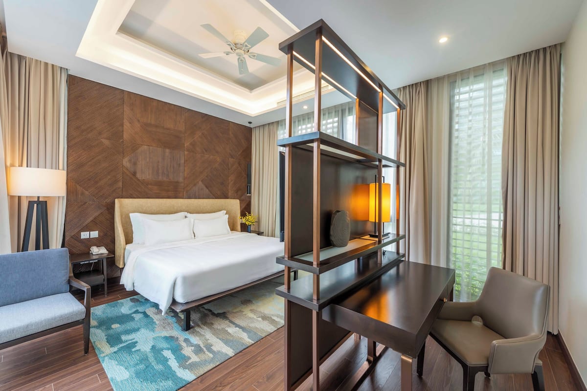 Une chambre d’hôtel équipée d’un lit, d’un bureau, d’une chaise, d’une lampe et d’un ventilateur de plafond.