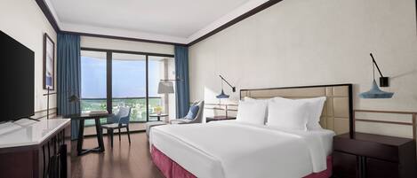 Habitación de hotel con una cama grande, un escritorio, una silla, un televisor y un balcón con vistas.