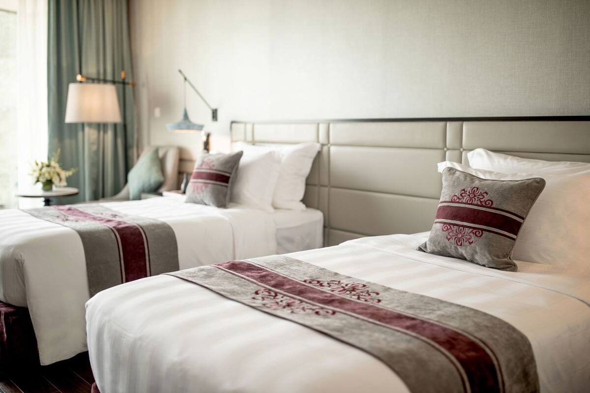 Une chambre d’hôtel avec deux lits, une table de chevet, une lampe et une vue sur l’extérieur.