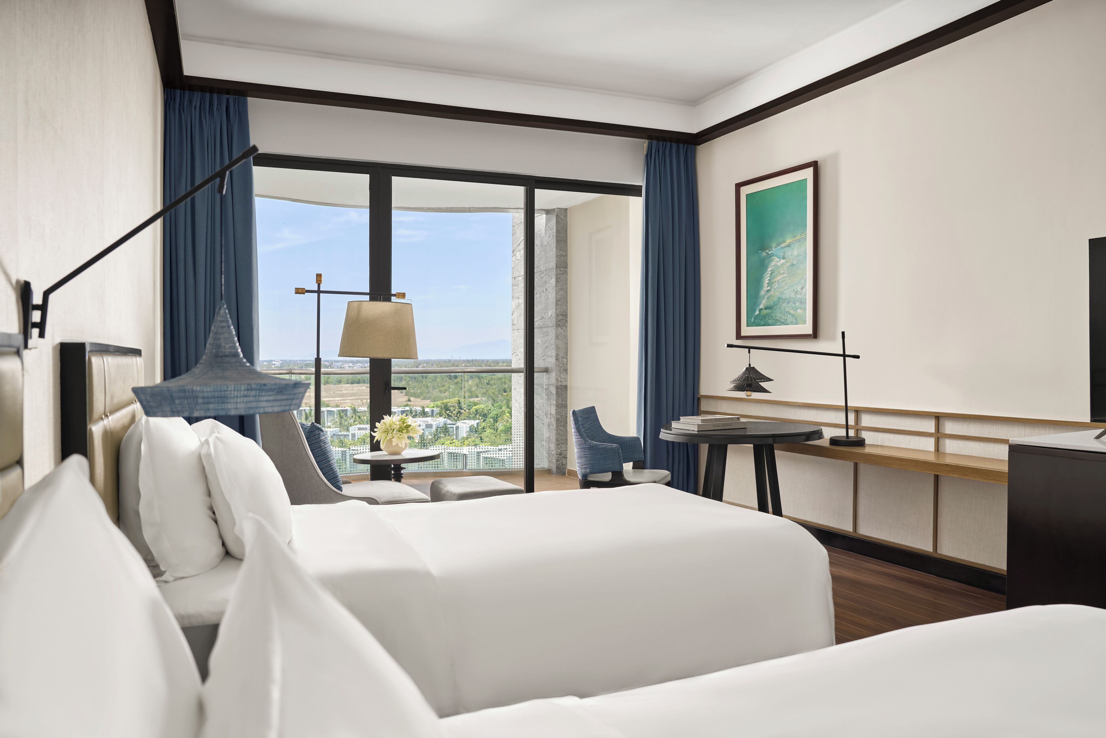 Une chambre d’hôtel avec un lit, un bureau, une chaise, une lampe et une vue sur le paysage urbain.