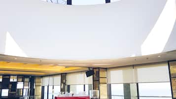 A modern bar area with a central red table, surrounded by seating and a glass display case.