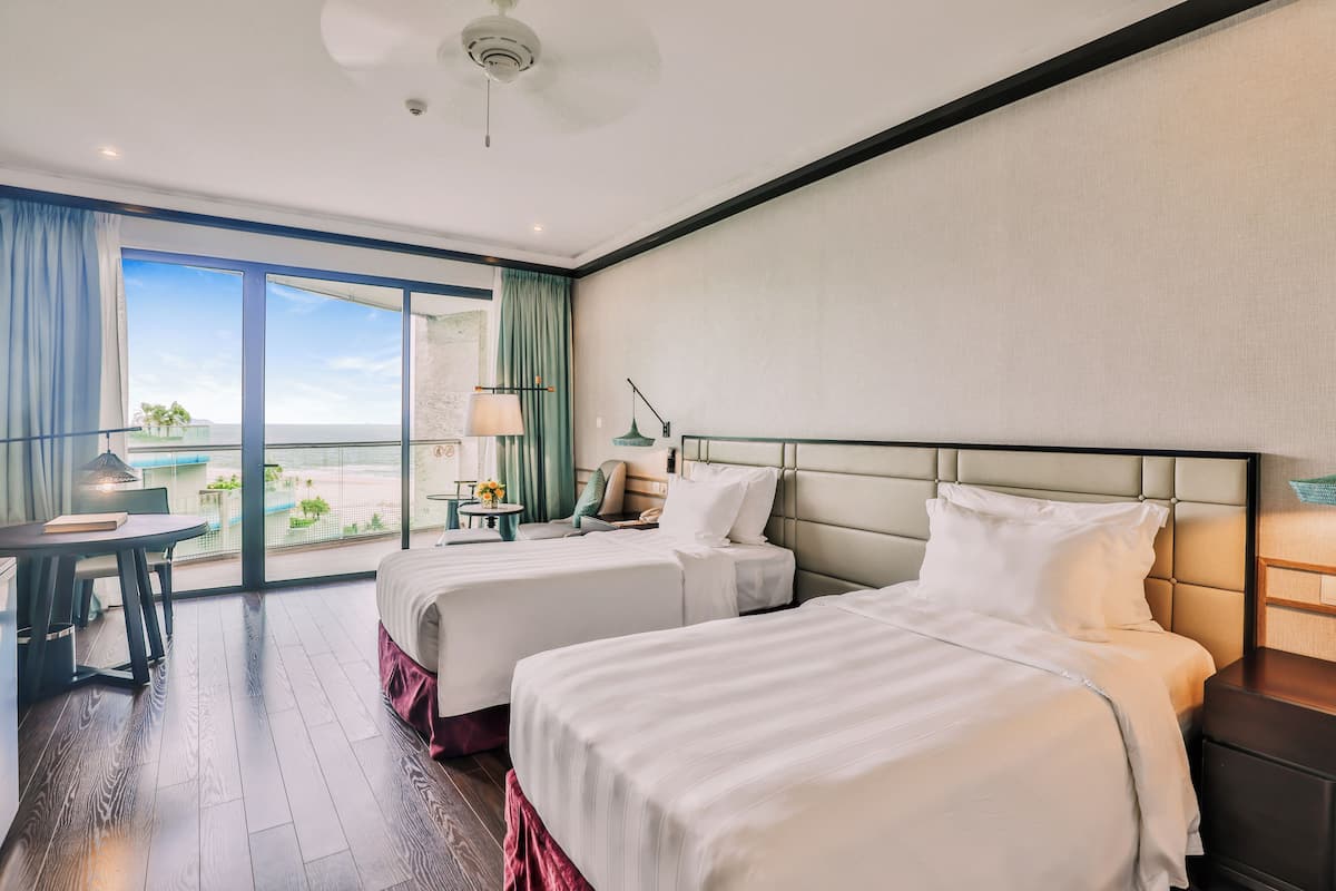 Une chambre d’hôtel avec deux lits, un bureau, une chaise, une lampe et une vue sur l’extérieur.