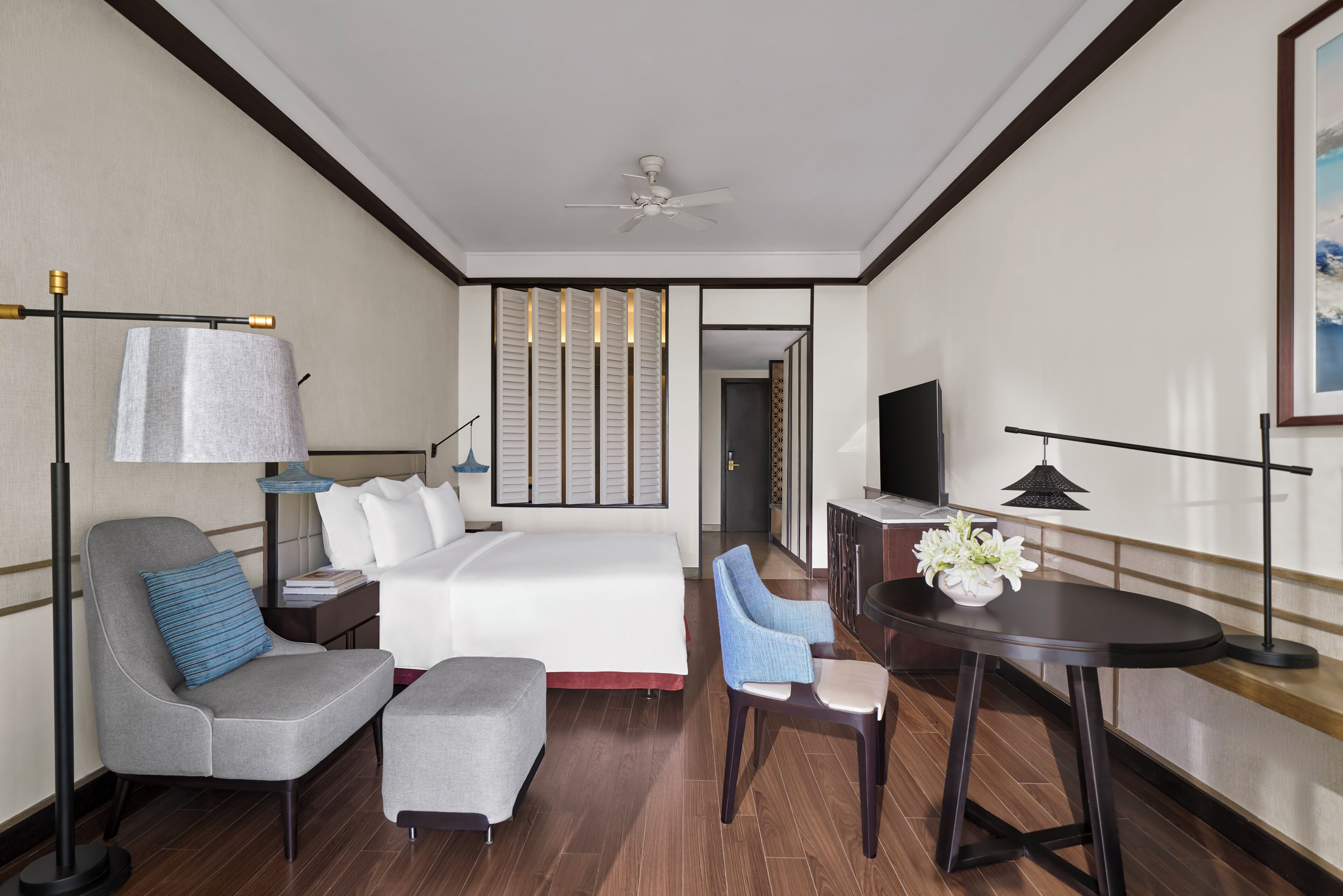 Une chambre d’hôtel équipée d’un lit, d’un bureau, d’une chaise, d’une télévision et d’un ventilateur de plafond.